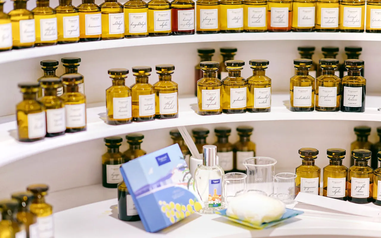 Wiele buteleczek z perfumami na półkach, jak w muzeum perfum w Paryżu. Zapachy w brązowych flakonach, niektóre z etykietami.