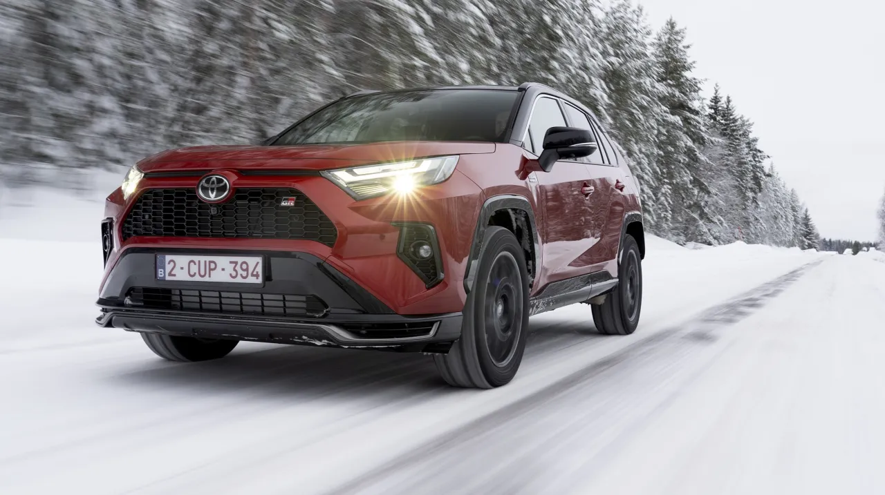 Czerwona Toyota RAV4 Hybrid GR Sport jedzie po zaśnieżonej drodze. Dowiedz się, ile kosztuje Toyota RAV4 Hybrid.