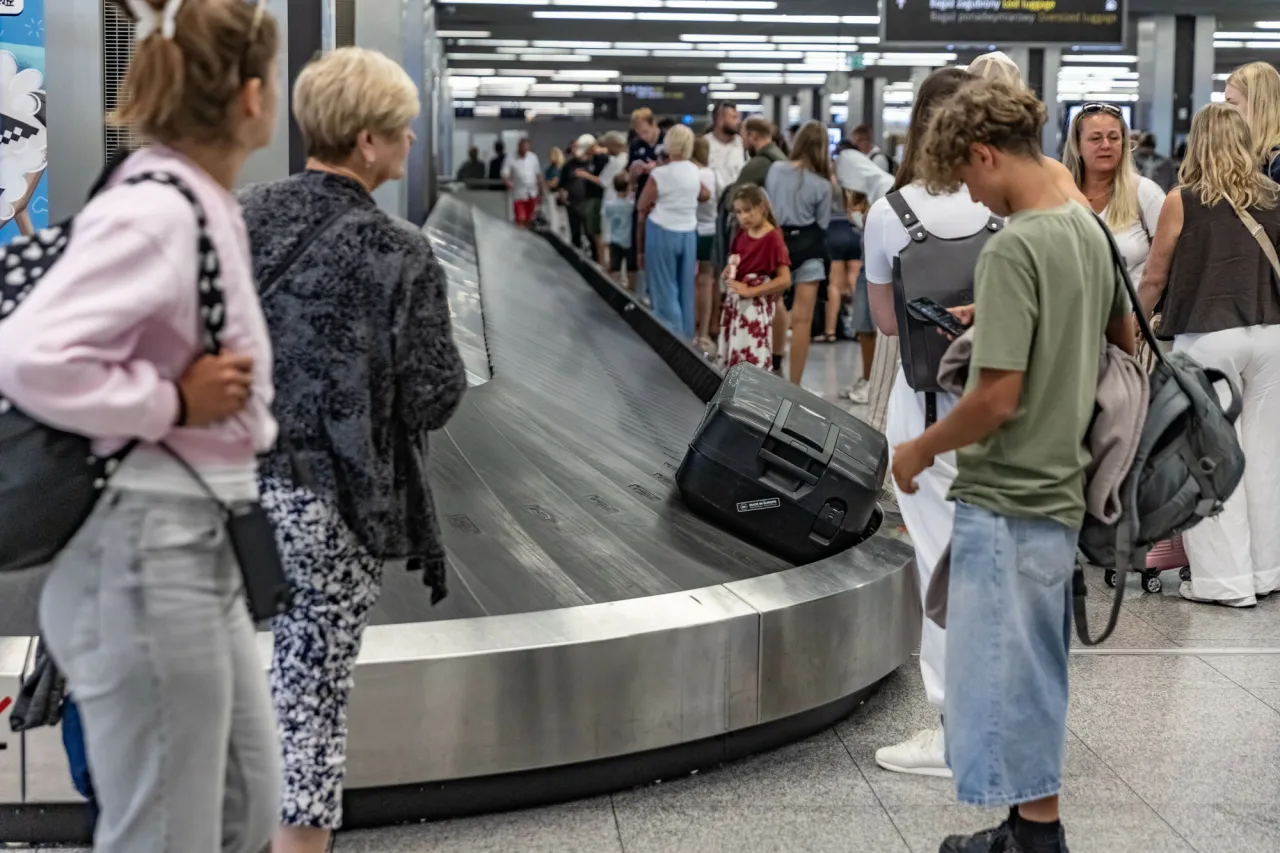 Ludzie czekają na bagaż na lotnisku. Zastanawiasz się, ile trzeba byc szybciej na lotnisku, by uniknąć tłoku przy odbiorze walizek.
