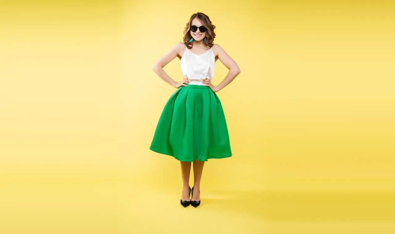 Kobieta w białej bluzce na ramiączkach i szerokiej, zielonej sp&oacute;dnicy. Idealna stylizacja: jaka bluzka do zielonej sp&oacute;dnicy?