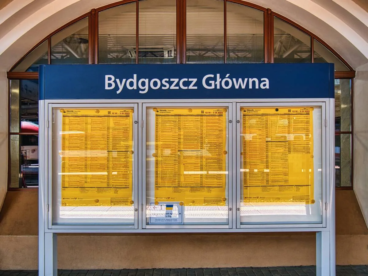 Rozkład jazdy PKP Bydgoszcz Główna. Trzy tablice z żółtymi rozkładami pociągów, widoczne na tle dworca.