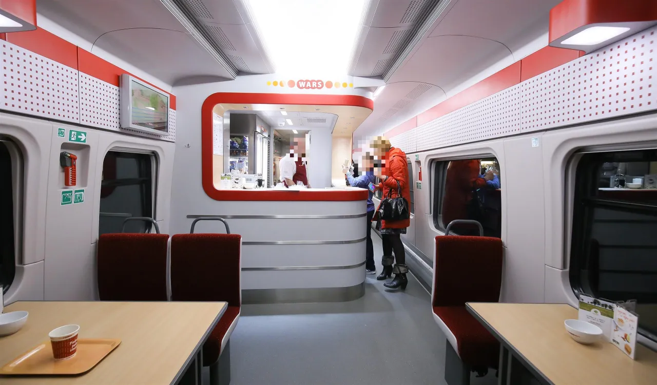 Wnętrze wagonu z miejscami do siedzenia i ladą gastronomiczną z napisem 