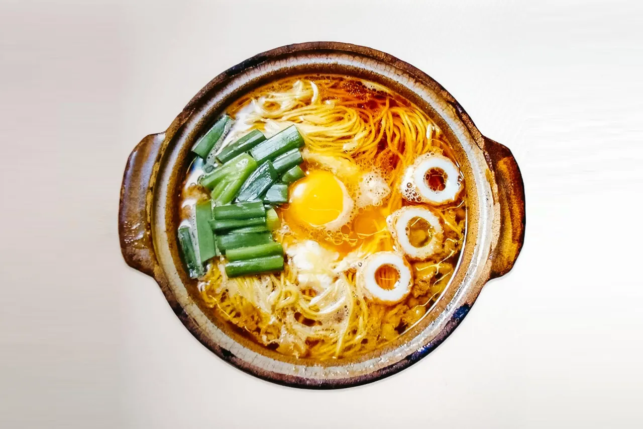 Aksamitny bulion, cienki makaron do ramen, jajko sadzone, zielona cebulka i rybne k&oacute;łka tworzą apetyczną kompozycję.