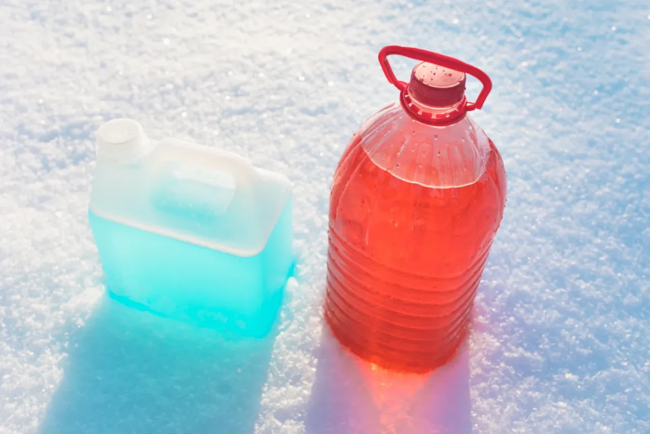 Płyn do spryskiwaczy na mrozie. Czy można myć okna zimą? Dwa płyny, niebieski i czerwony, leżą na śniegu.