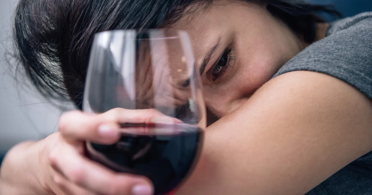 Osoba zastanawiająca się nad problemem alkoholowym, z kieliszkiem wina w dłoni, ale z zamyśloną miną
