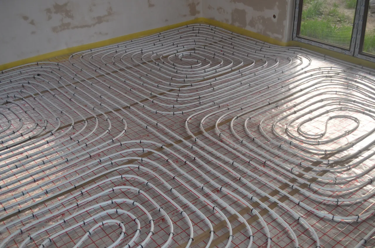 Instalacja ogrzewania podłogowego bez wylewki. Białe rurki ułożone na siatce izolacyjnej tworzą spiralne wzory, gotowe do zatopienia w podłodze.