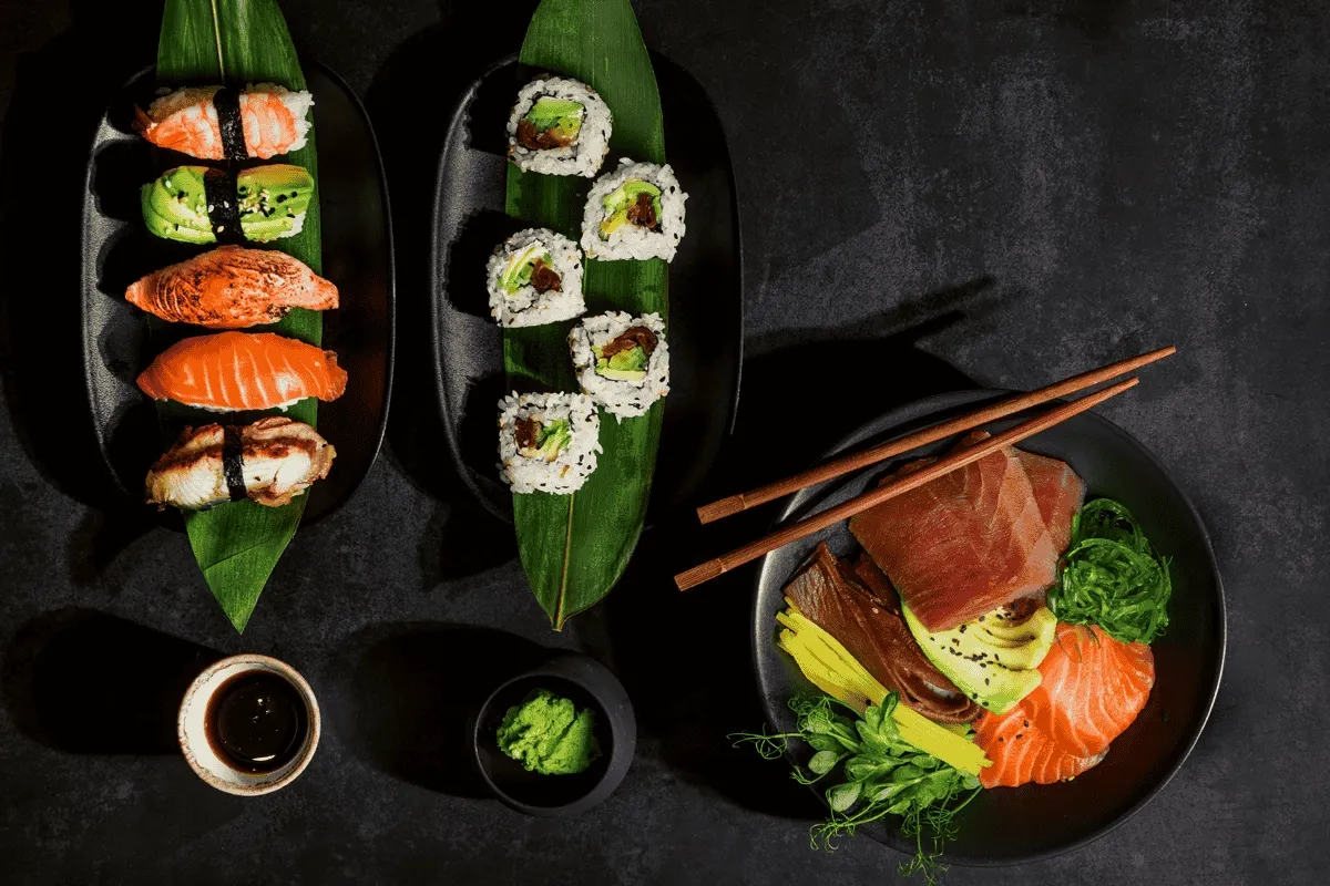 Wykwintne chirashi zushi z łososiem, awokado i krewetkami, obok rolki sushi i miseczki z tuńczykiem, wodorostami i warzywami.