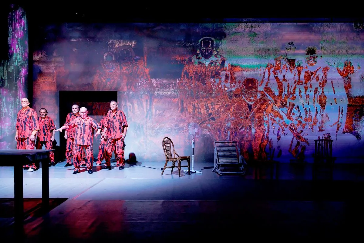 Aktorzy w czerwono-czarnych strojach na scenie. Jan Klata reżyseruje teatr pełen surrealistycznych projekcji.