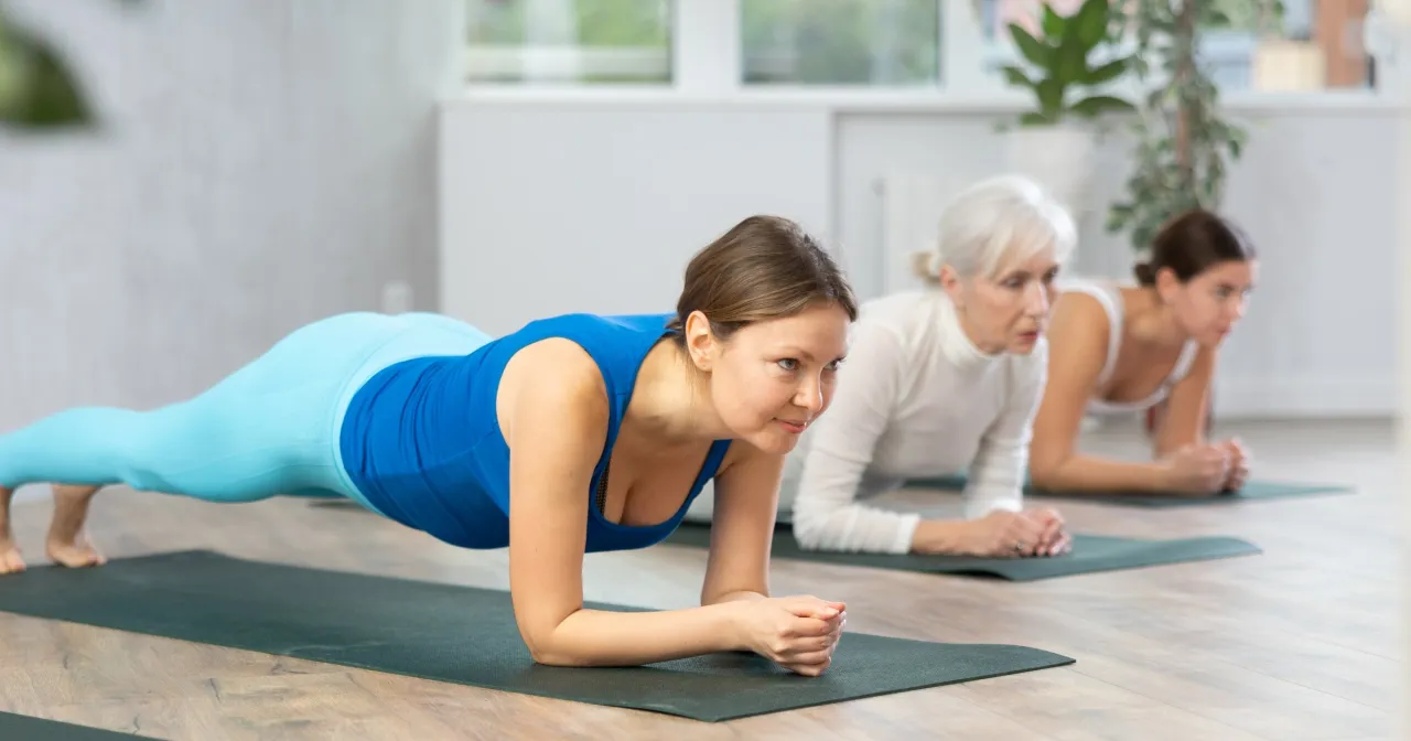 Trzy kobiety wykonują deskę. To ćwiczenie może być pomocne w rehabilitacji po złamaniu kręgosłupa lędźwiowego.