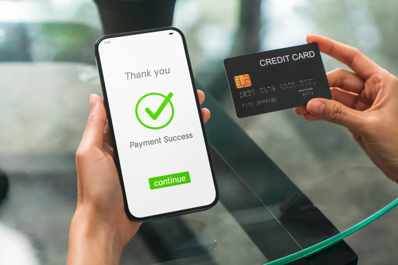 Dłoń trzyma smartfon z potwierdzeniem płatności i kartę kredytową. Czy lokata mobilna jest bezpieczna? Tak, transakcje są chronione.