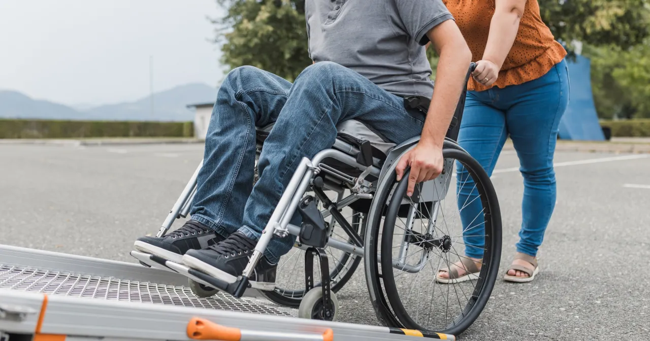 Osoba na wózku inwalidzkim zjeżdża po rampie. Warto wiedzieć, ile wynosi renta niepełnosprawnych, by zapewnić godne życie.