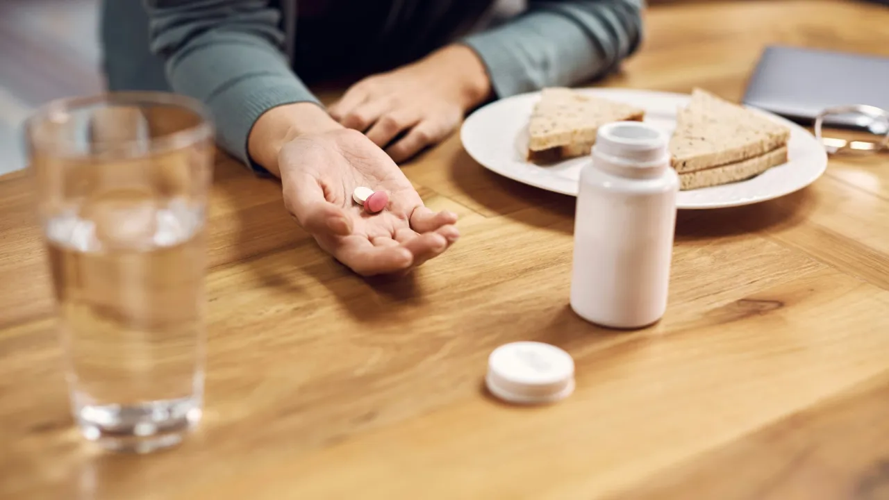 Dłoń z tabletkami, szklanka wody, kanapka i buteleczka leków. Jak obniżyć poziom greliny?