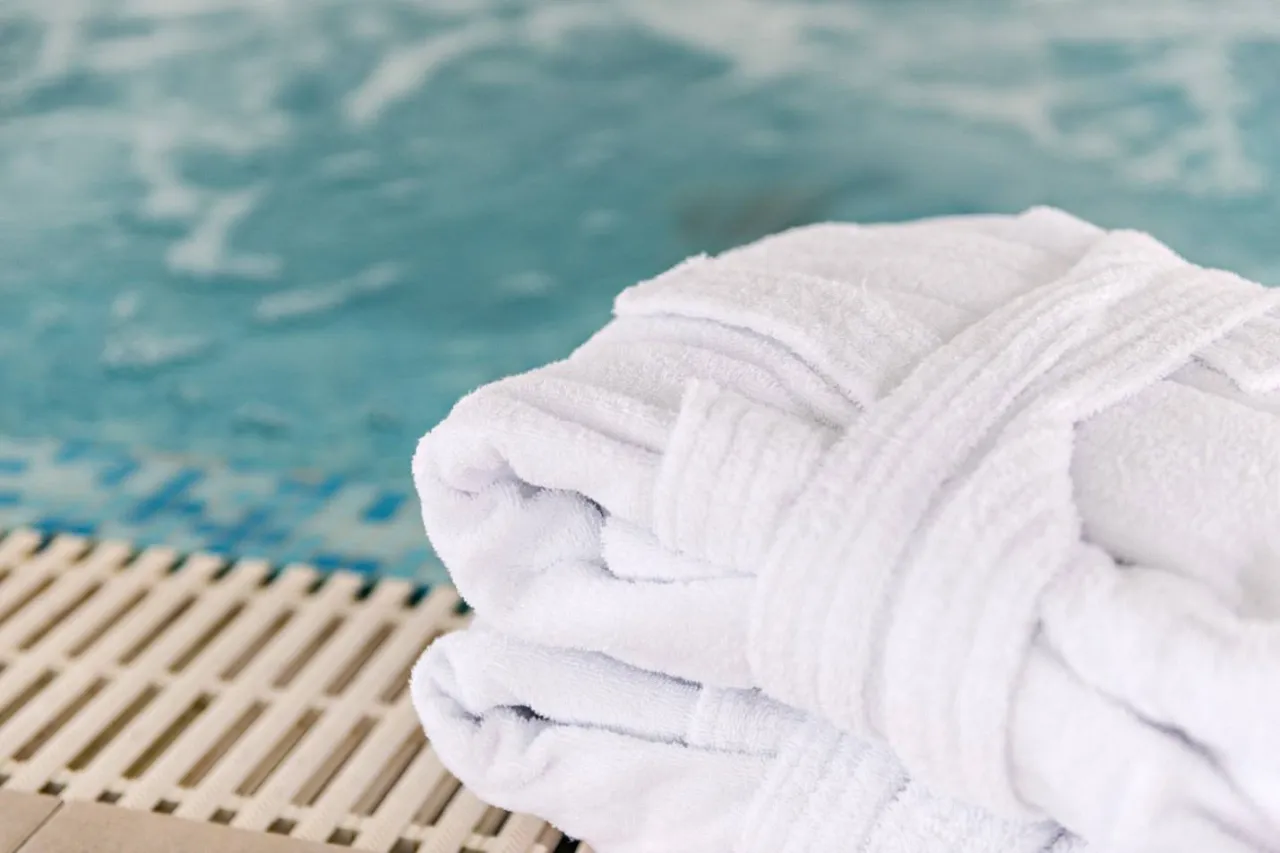 Biały szlafrok i ręcznik przy basenie. Idealne rzeczy, co zabrać na termy zimą, by poczuć komfort.