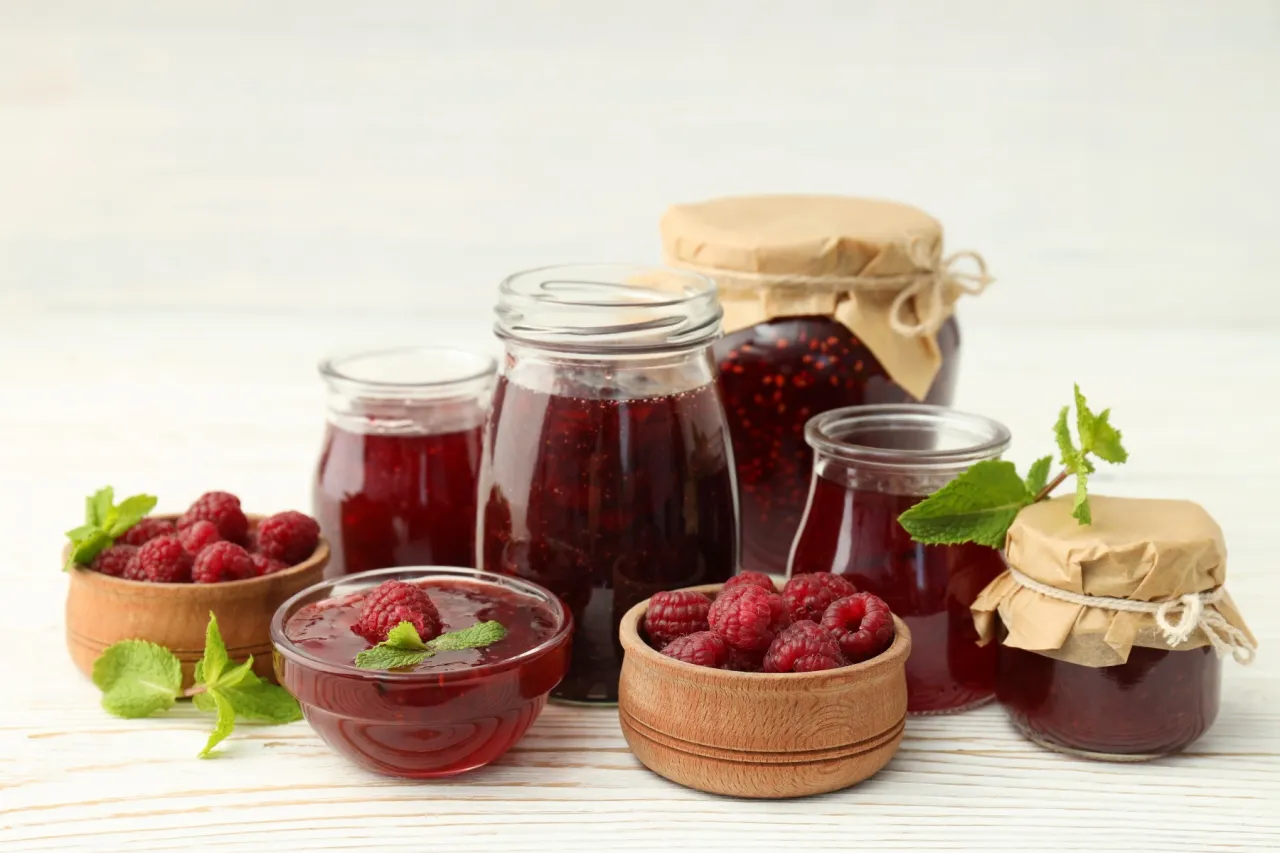 Słoiki z domowym dżemem malinowym i świeże maliny. Idealne, by pokazać, jak zrobić sok z malin na surowo.