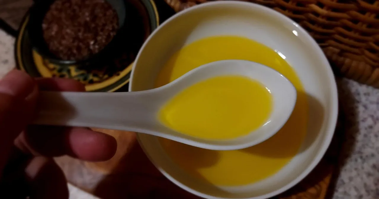 Łyżka oleju lnianego, który może pomóc obniżyć cholesterol. W tle widać miseczkę z czymś ciemnym.