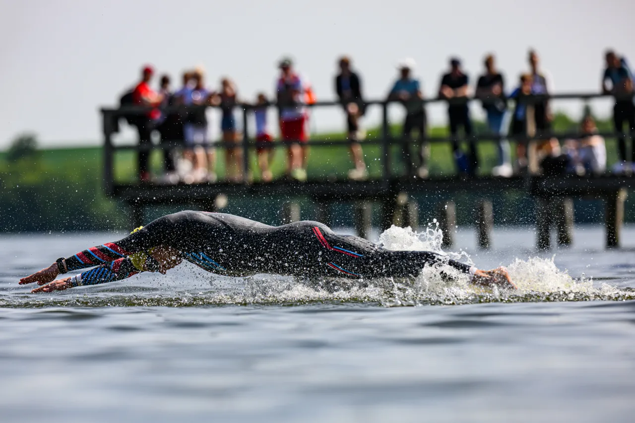 Pływak w kombinezonie zanurza się w wodzie, tworząc rozpryski. To przykład, co to jest trening aerobowy, poprawiający wydolność.