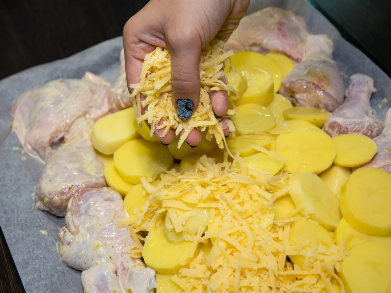 Ręka sypie starty ser na kurczaka i ziemniaki. Idealny pomysł, co zrobić jutro na obiad!