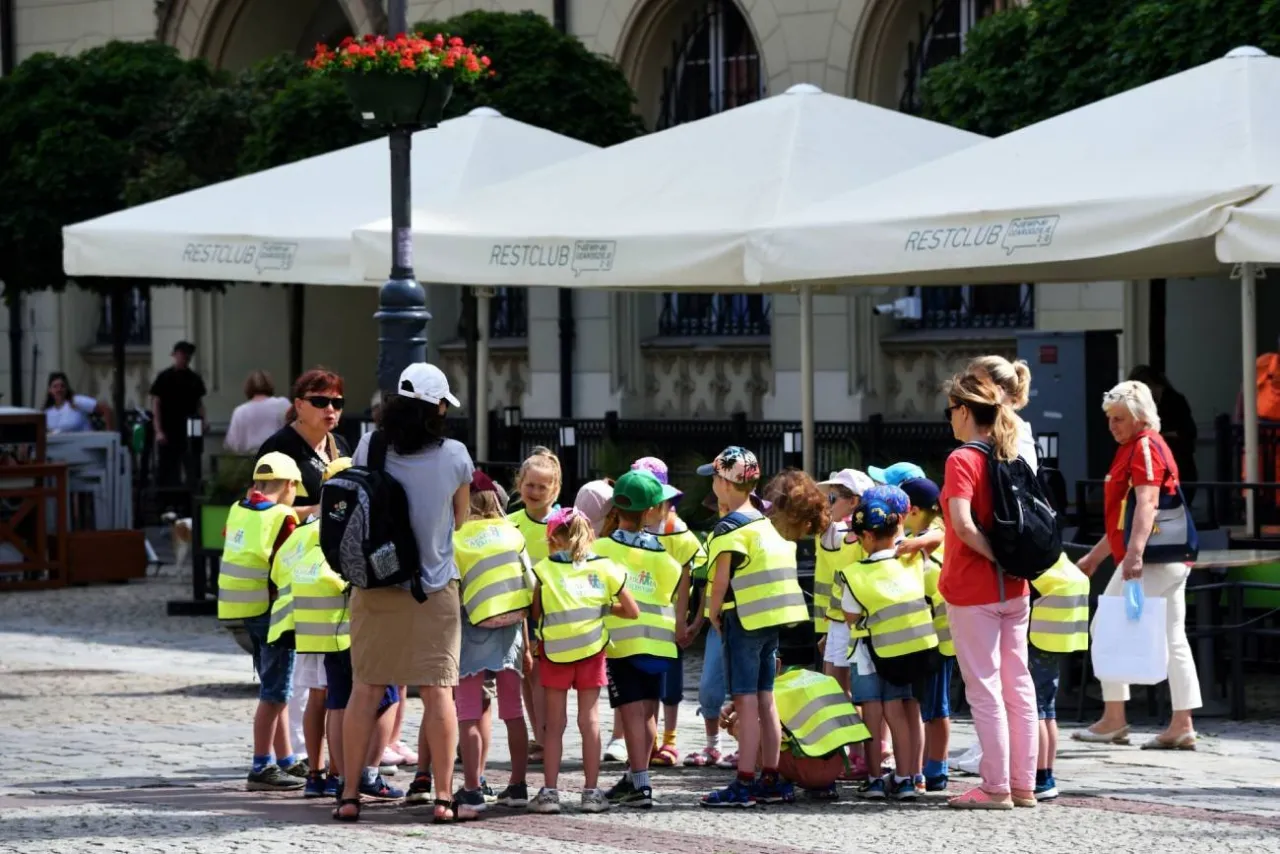 Grupa dzieci w kamizelkach odblaskowych, z opiekunami. Niska liczba dzieci na jednego opiekuna zapewnia bezpieczeństwo.