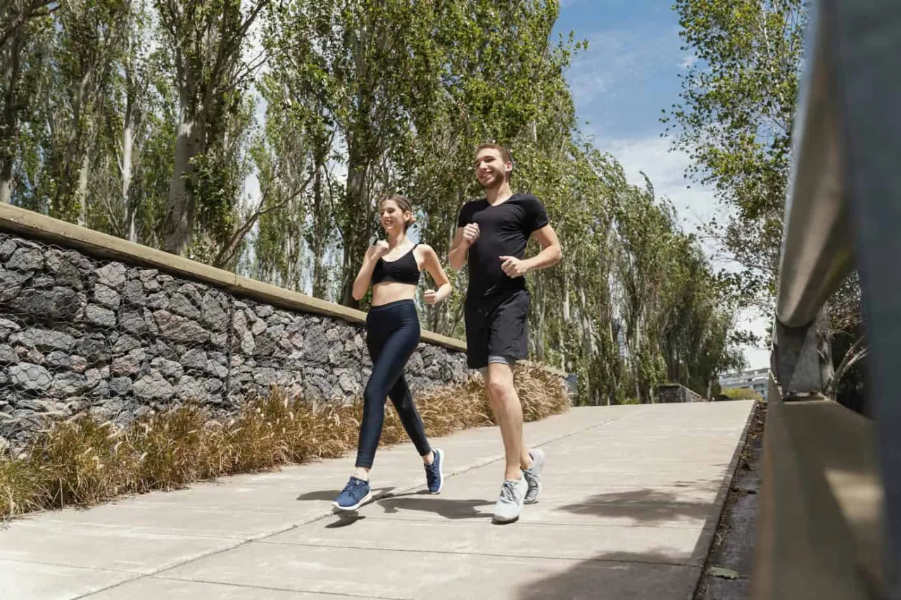Para schudnąć 1 kg, trzeba ćwiczyć regularnie. Młoda para biegnie ścieżką wśr&oacute;d drzew, ciesząc się aktywnością fizyczną.