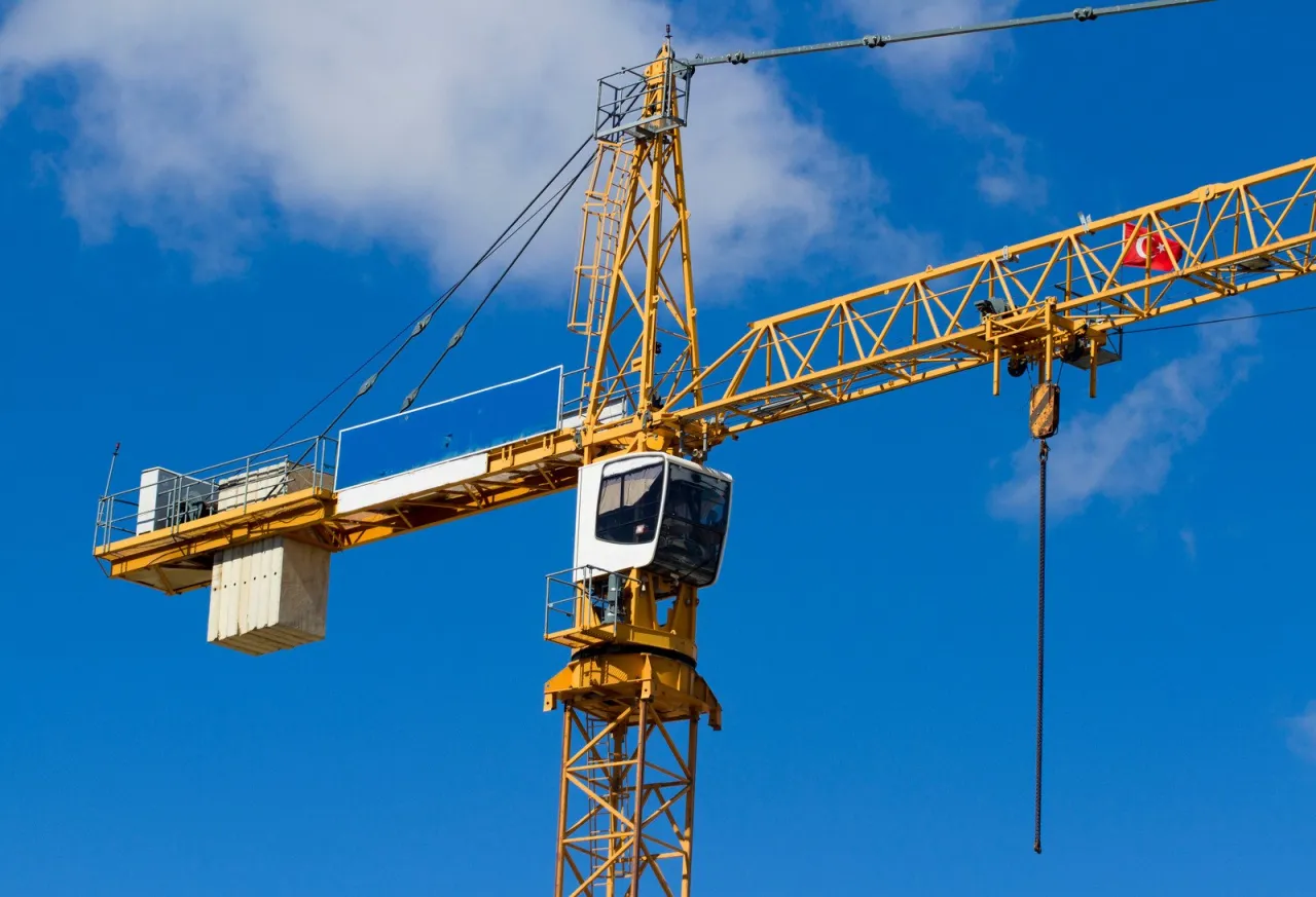 Ż&oacute;łty dźwig budowlany na tle błękitnego nieba z chmurami. To co to jest dźwig, widać jego kabinę operatora i wysięgnik.