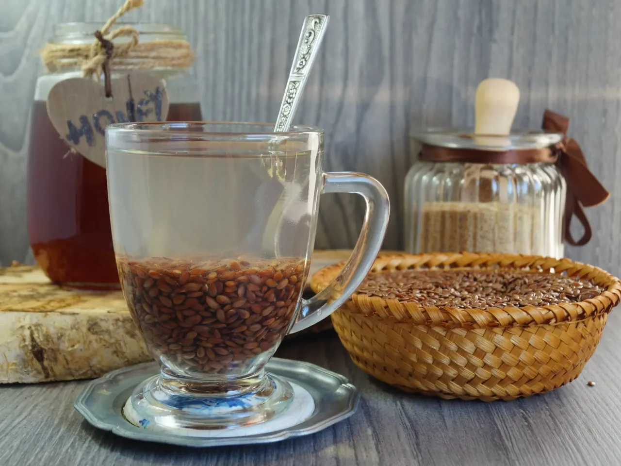 Naczynie z wodą i siemieniem lnianym, obok mi&oacute;d i koszyk z nasionami. Czy od siemienia lnianego się tyje? To pytanie nurtuje wiele os&oacute;b.