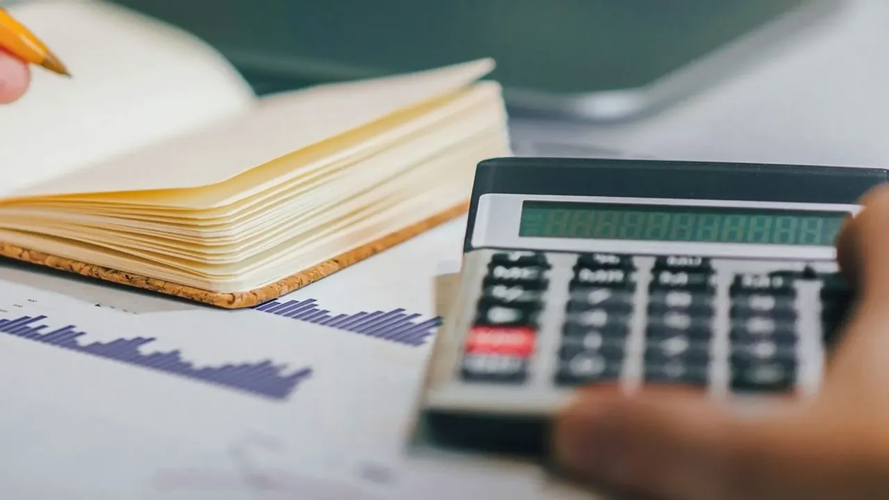 Dłoń trzyma kalkulator, obok leży otwarty notatnik i wykres. Czy bezrobocie wlicza się do lat pracy?