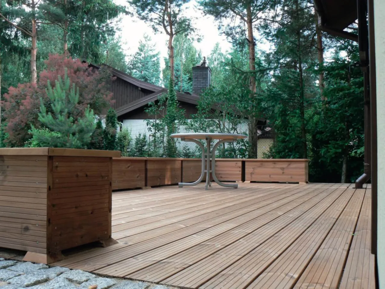 Drewniany taras z donicami i stołem. Zastanawiasz się, ile kosztuje budowa tarasu drewnianego?