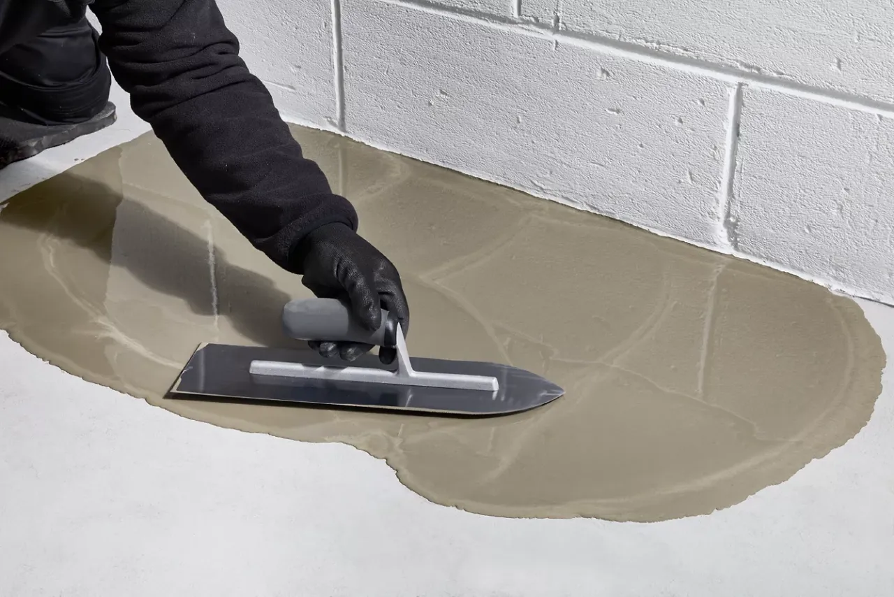 Ręka w rękawicy wygładza świeżą wylewkę betonową kielnią. Dowiedz się, jak zrobić wylewkę betonową krok po kroku.