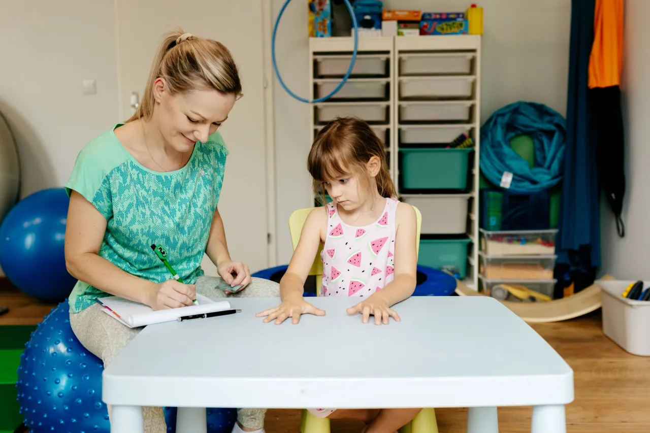 Rodzic robiący notatki o zachowaniu dziecka, dziecko bawiące się z terapeutą SI
