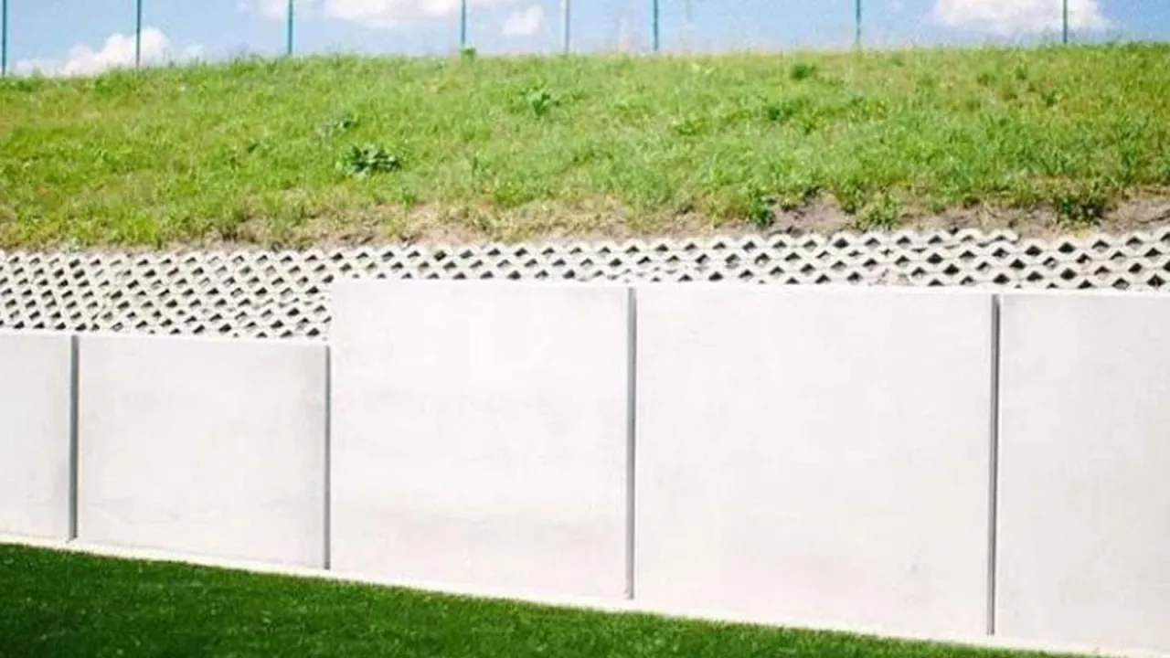 Nowoczesny mur oporowy z betonowych płyt, podtrzymujący zielone zbocze. Dowiedz się, jak uzyskać pozwolenie na budowę muru oporowego.