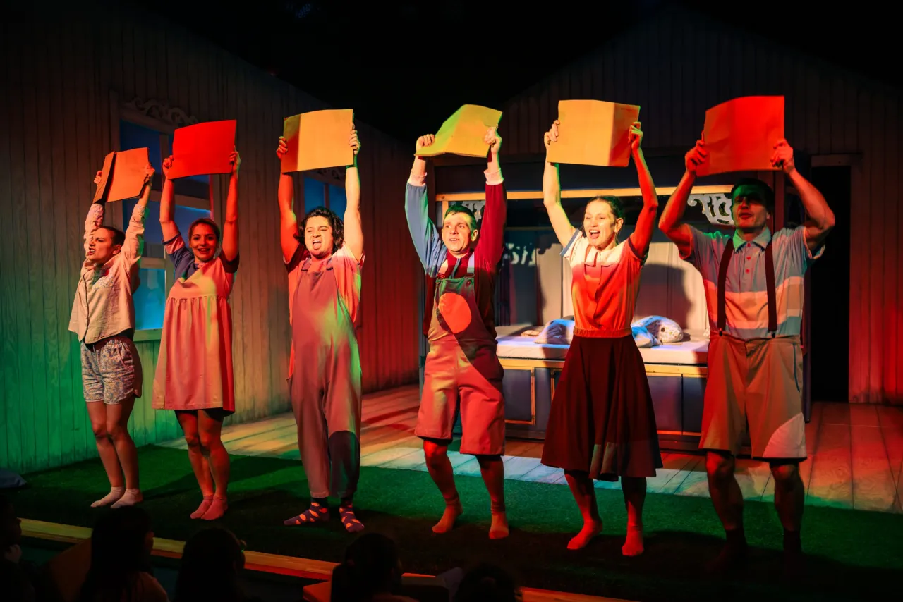 Aktorzy w kolorowych strojach podczas przedstawienia teatralnego dla dzieci, trzymający w górze kartony.