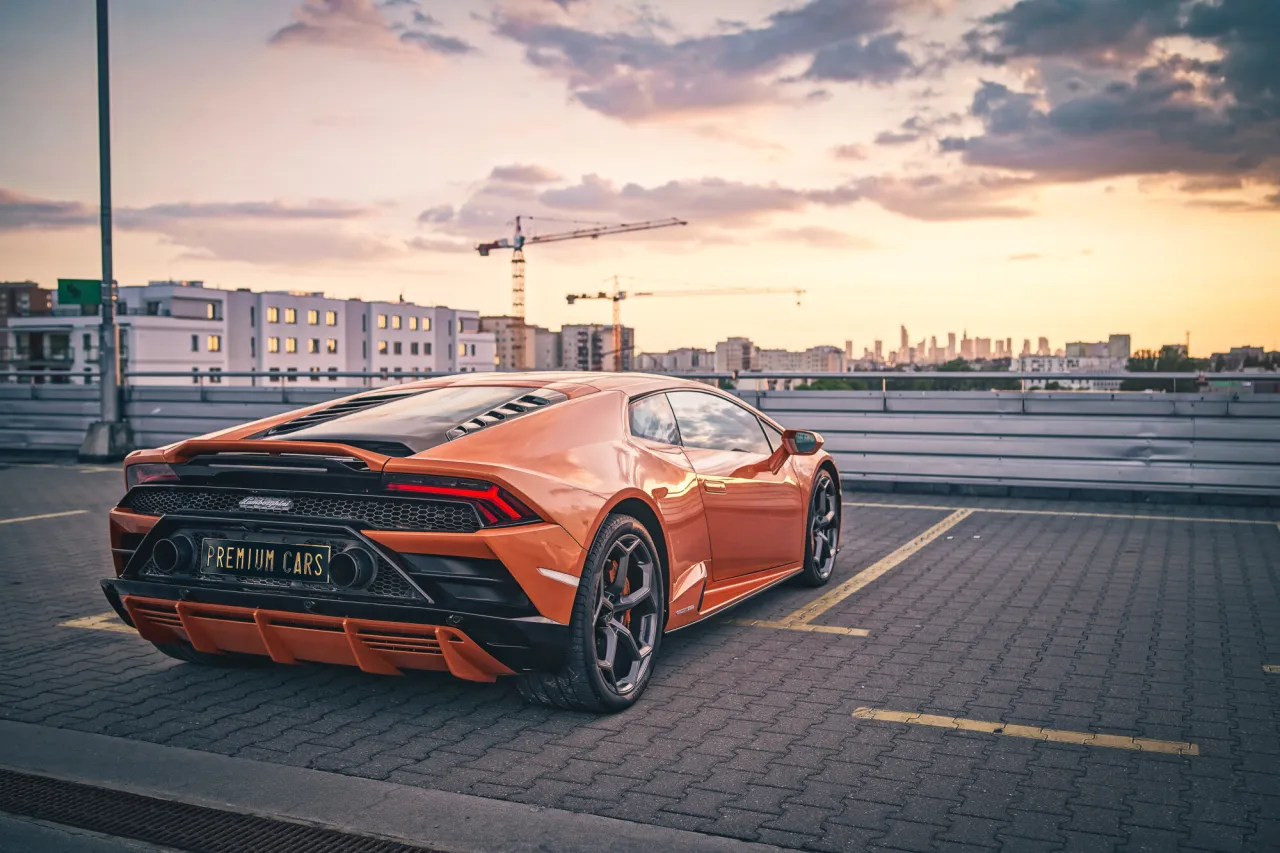 Pomarańczowe Lamborghini na parkingu, zach&oacute;d słońca. Zastanawiasz się, ile kosztuje wypożyczenie lamborghini?