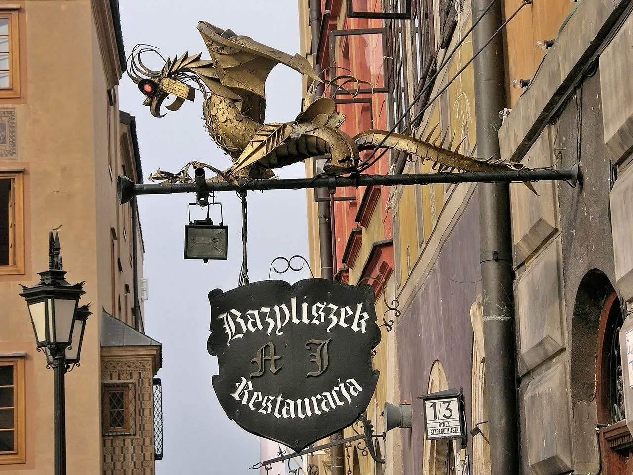 Złoty bazyliszek wisi nad szyldem restauracji, przypominając legendę o tym mitycznym stworzeniu.