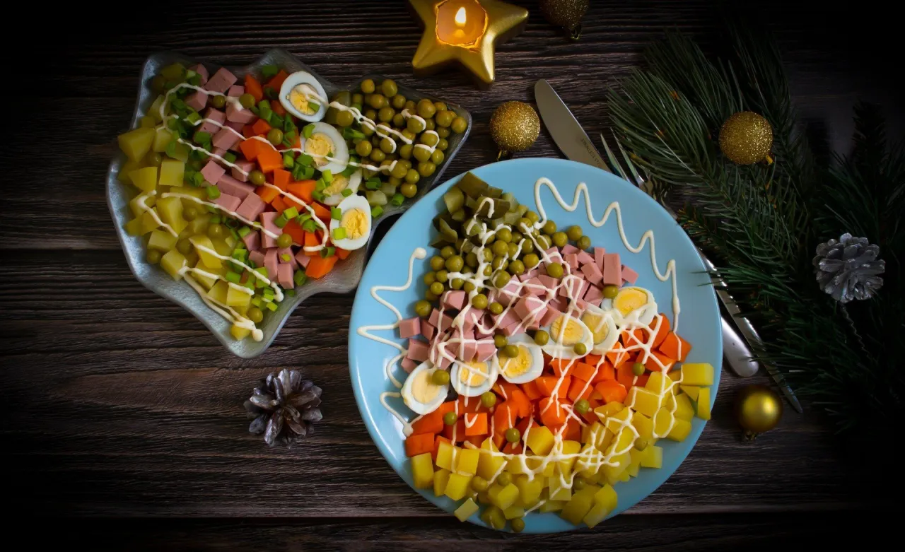 Sałatka jarzynowa na talerzu, idealna odpowiedź na pytanie co ugotować na święta. Obok miska z tą samą potrawą, ozdoby świąteczne.