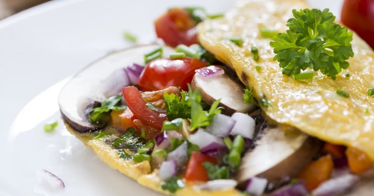 Omlet z pieczarkami, pomidorkami i cebulką to idealna wysokobiałkowa kolacja.