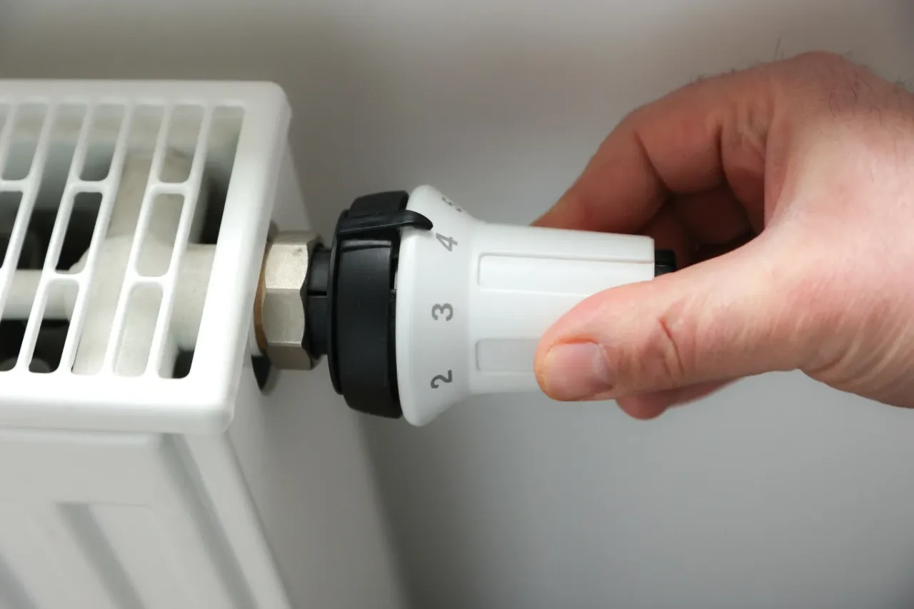 Dłoń reguluje termostat grzejnika, ustawiając temperaturę. Czekamy na okres grzewczy w blokach.