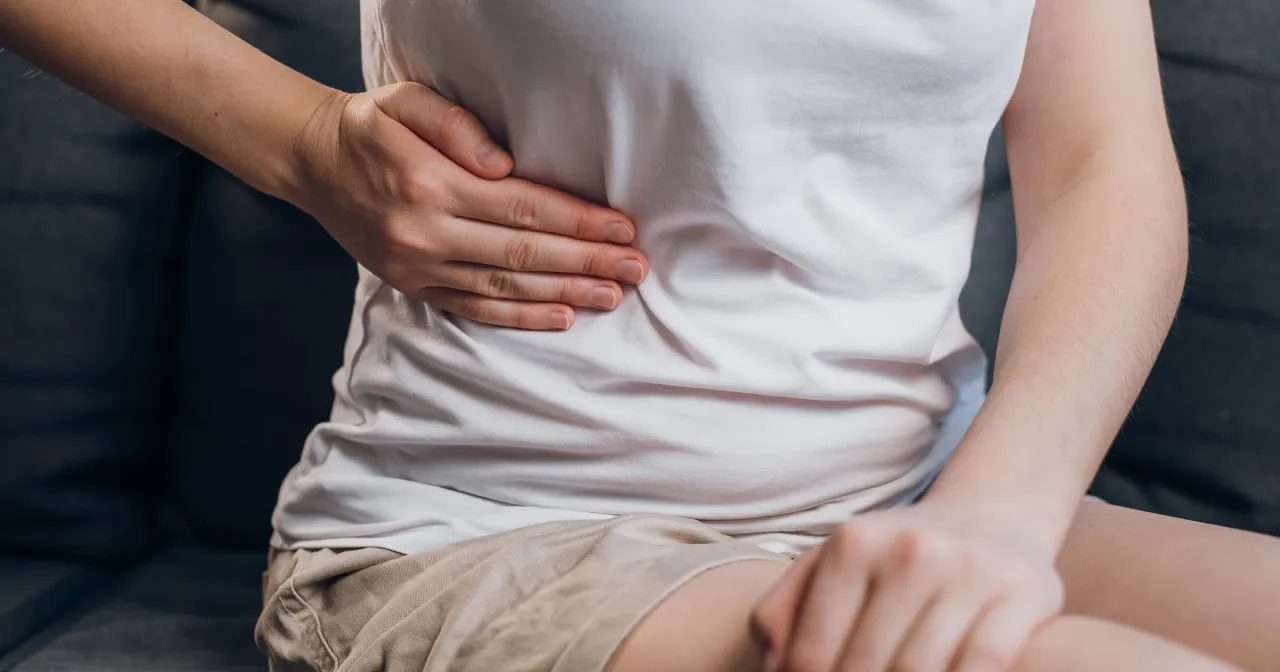 Osoba trzyma się za brzuch, szukając ulgi. Zastanawia się, co pomaga na b&oacute;l brzucha, by poczuć się lepiej.