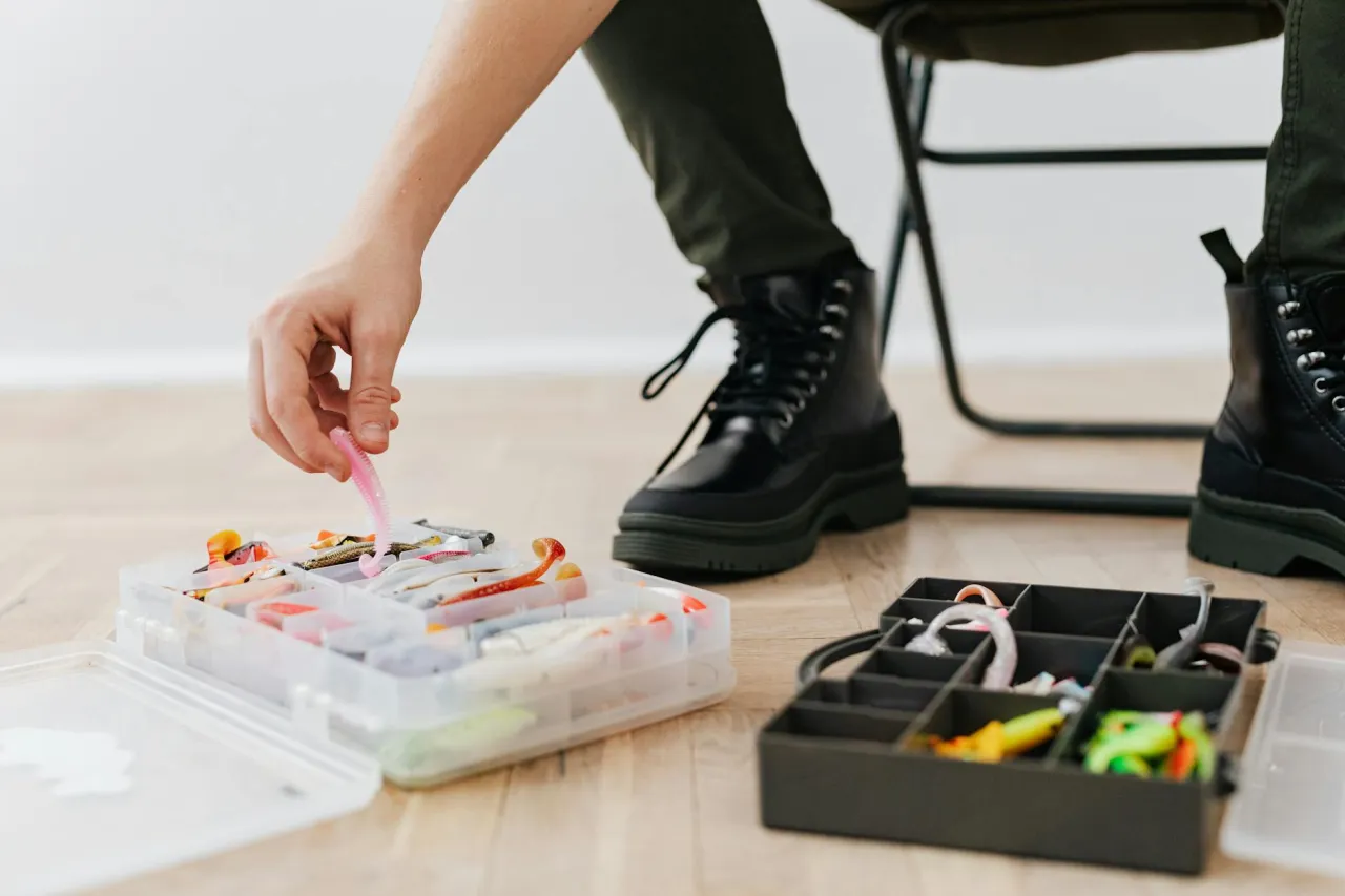 Dłoń wybiera różowego robaka z pudełka, pokazując, jak przechowywać robaki na ryby.