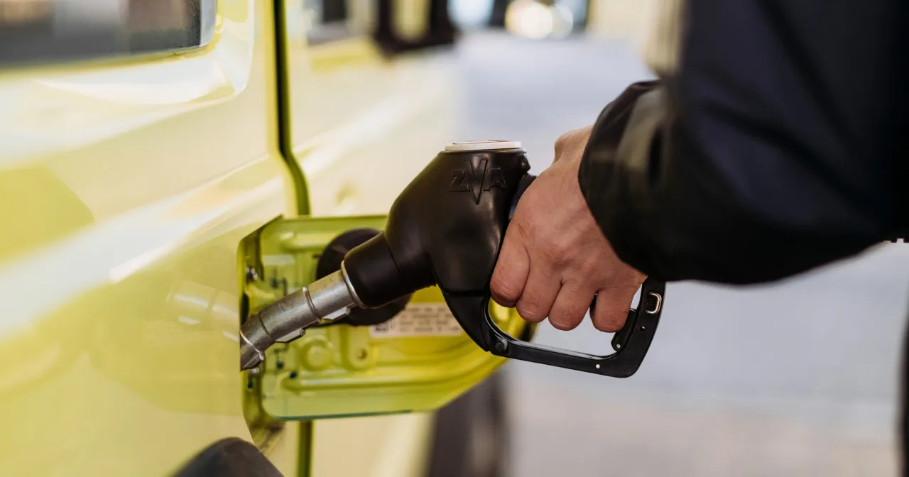 Dłoń trzymająca pistolet paliwowy przy żółtym samochodzie. Szukasz, gdzie najlepsze paliwo?