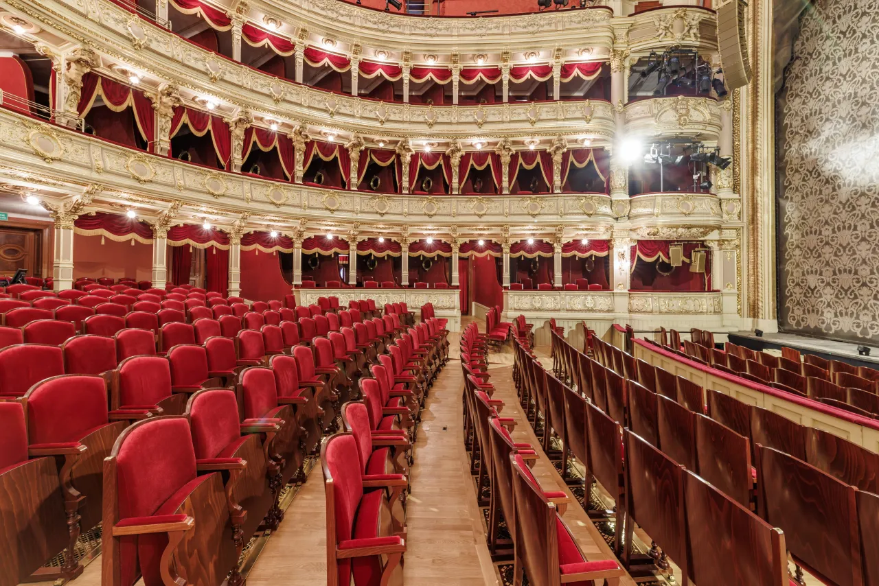 Elegancka sala teatralna z czerwonymi fotelami i złotymi zdobieniami. Idealne miejsce, by sprawdzić, na co warto iść do teatru w Krakowie.