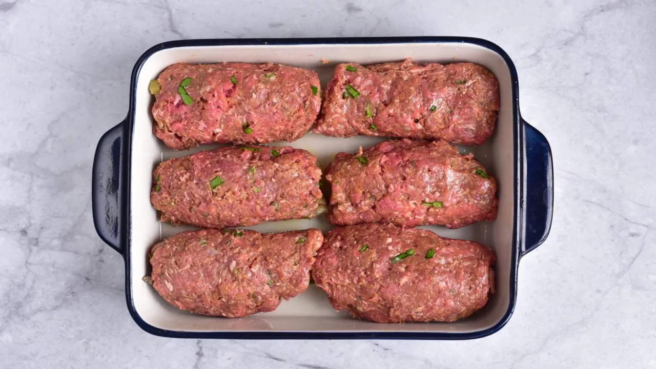 Sześć podłużnych kotletów z mięsa mielonego z zielonymi dodatkami, gotowych do pieczenia. Idealne pytanie: co ugotować z mięsa mielonego?
