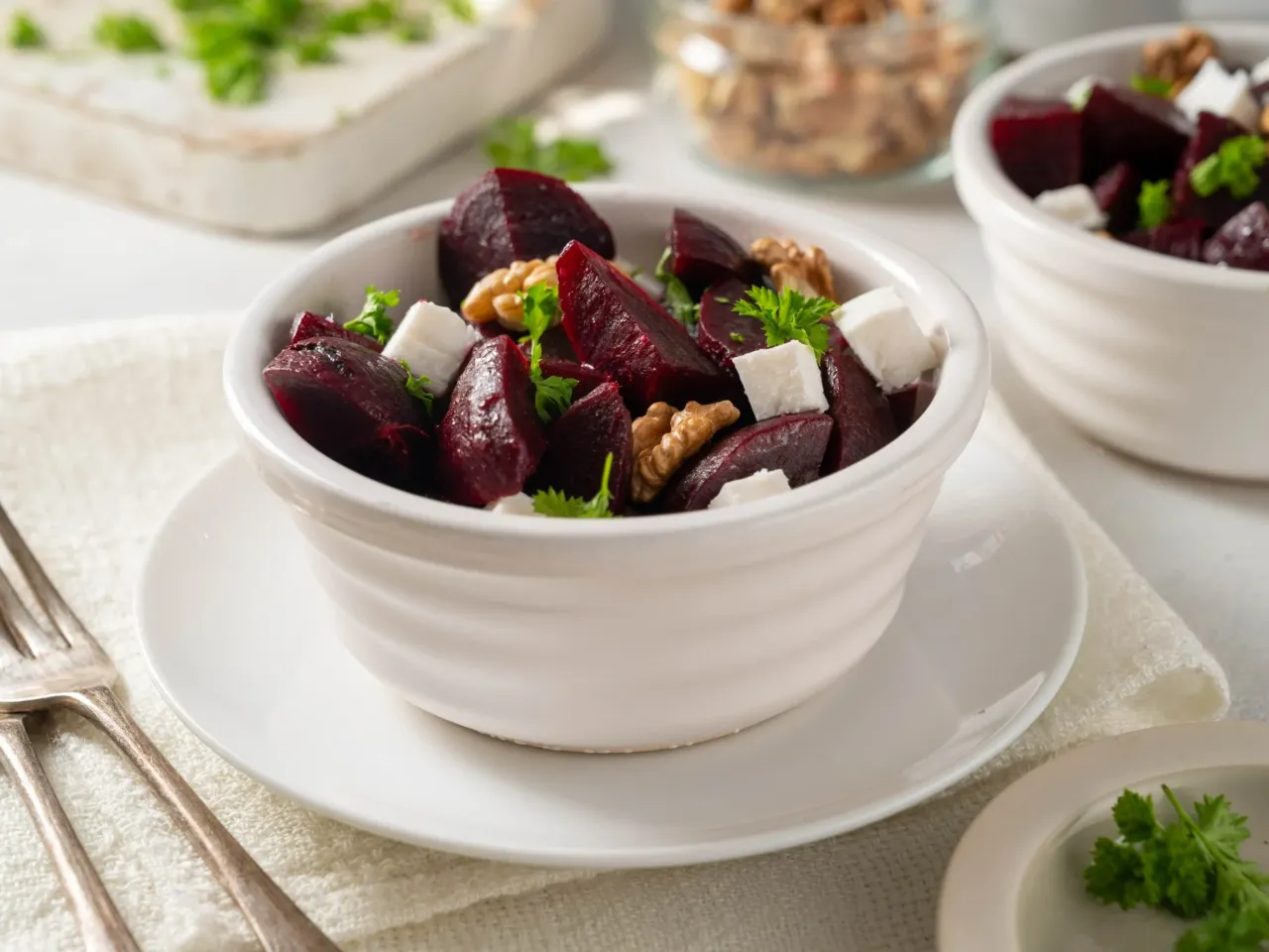 Sałatka z burakami i fetą, orzechami włoskimi i natką pietruszki w białej miseczce.