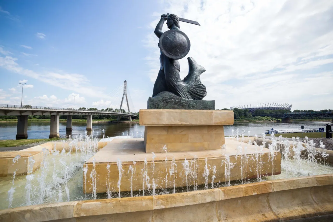 Pomnik Syrenki Warszawskiej, symbol legendy o Warsie i Sawie, na tle Wisły i most&oacute;w.