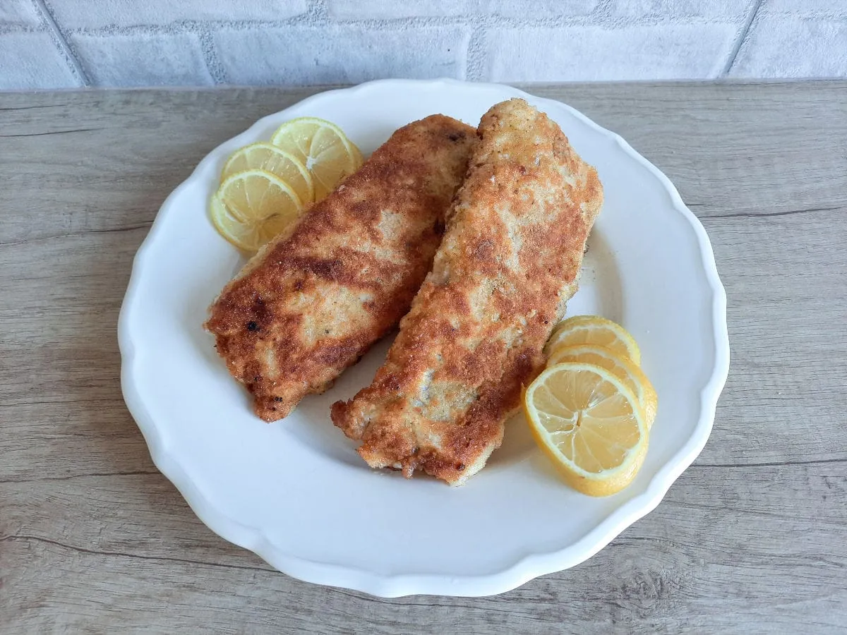 Dwie panierowane ryby na talerzu z plasterkami cytryny. Idealne, gdy zastanawiasz się, jak usmażyć dietetyczną rybę.