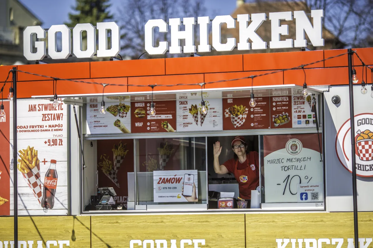 Stacja paliw Good Chicken z menu pełnym kurczaków, frytek i burgerów. Pracownica macha do klientów.