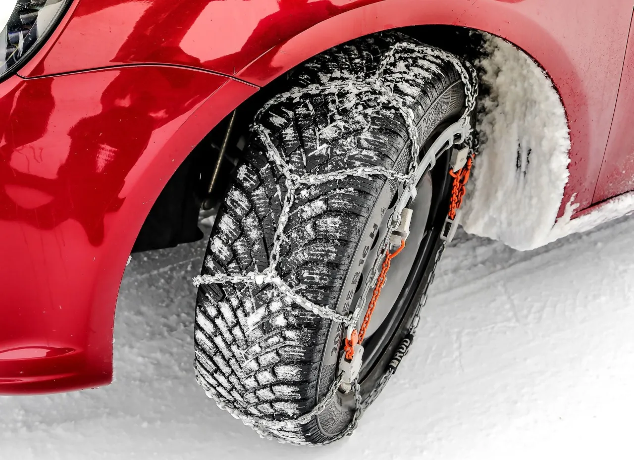Czerwony samoch&oacute;d na śniegu z założonymi łańcuchami na koło. Uniknij mandatu za brak łańcuch&oacute;w w Polsce.