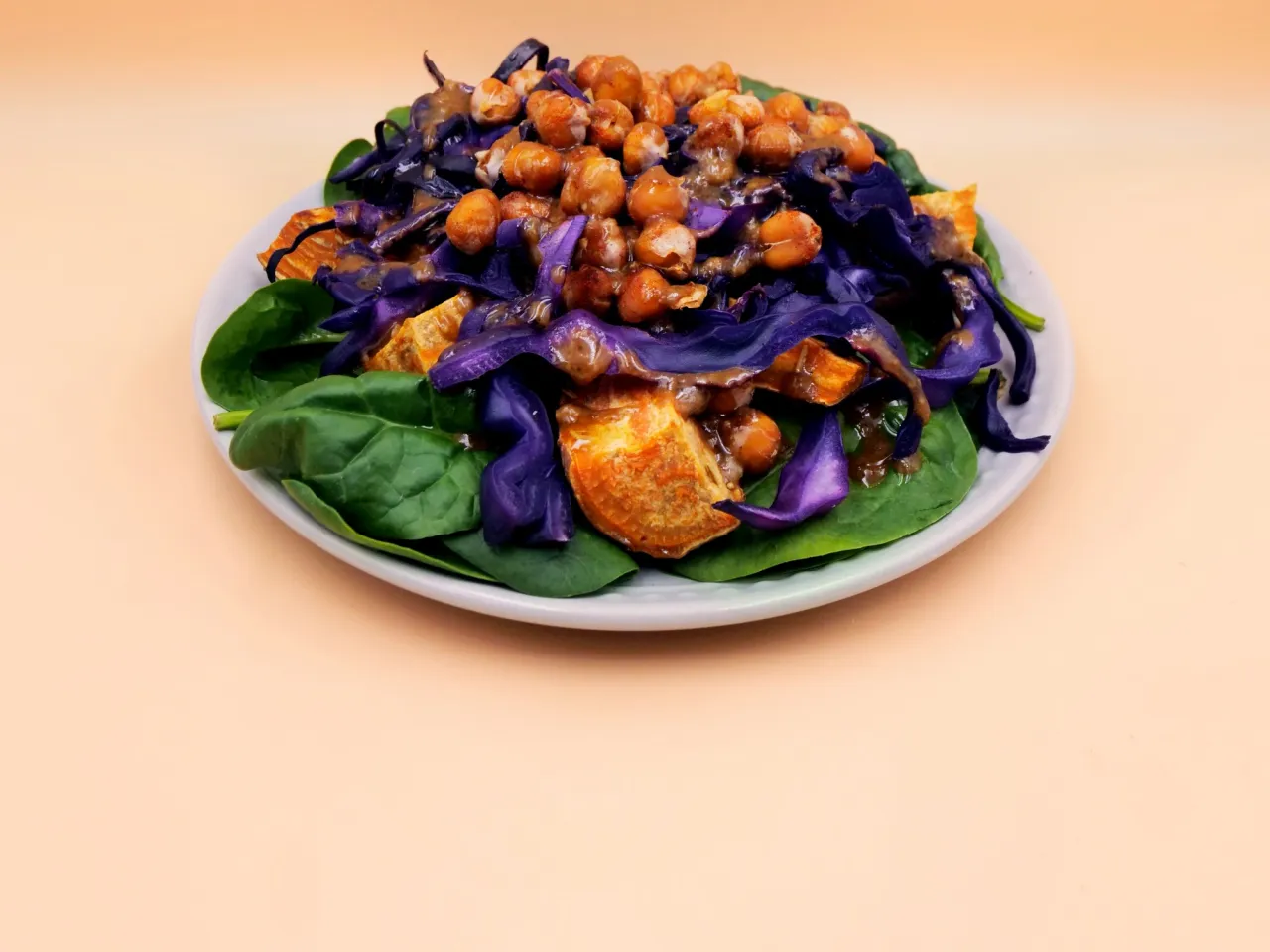 Kolorowa sałatka z ciecierzycy, pieczonych batatów i czerwonej kapusty na liściach szpinaku. Idealna jako jaka sałatka do gęsi pieczonej.