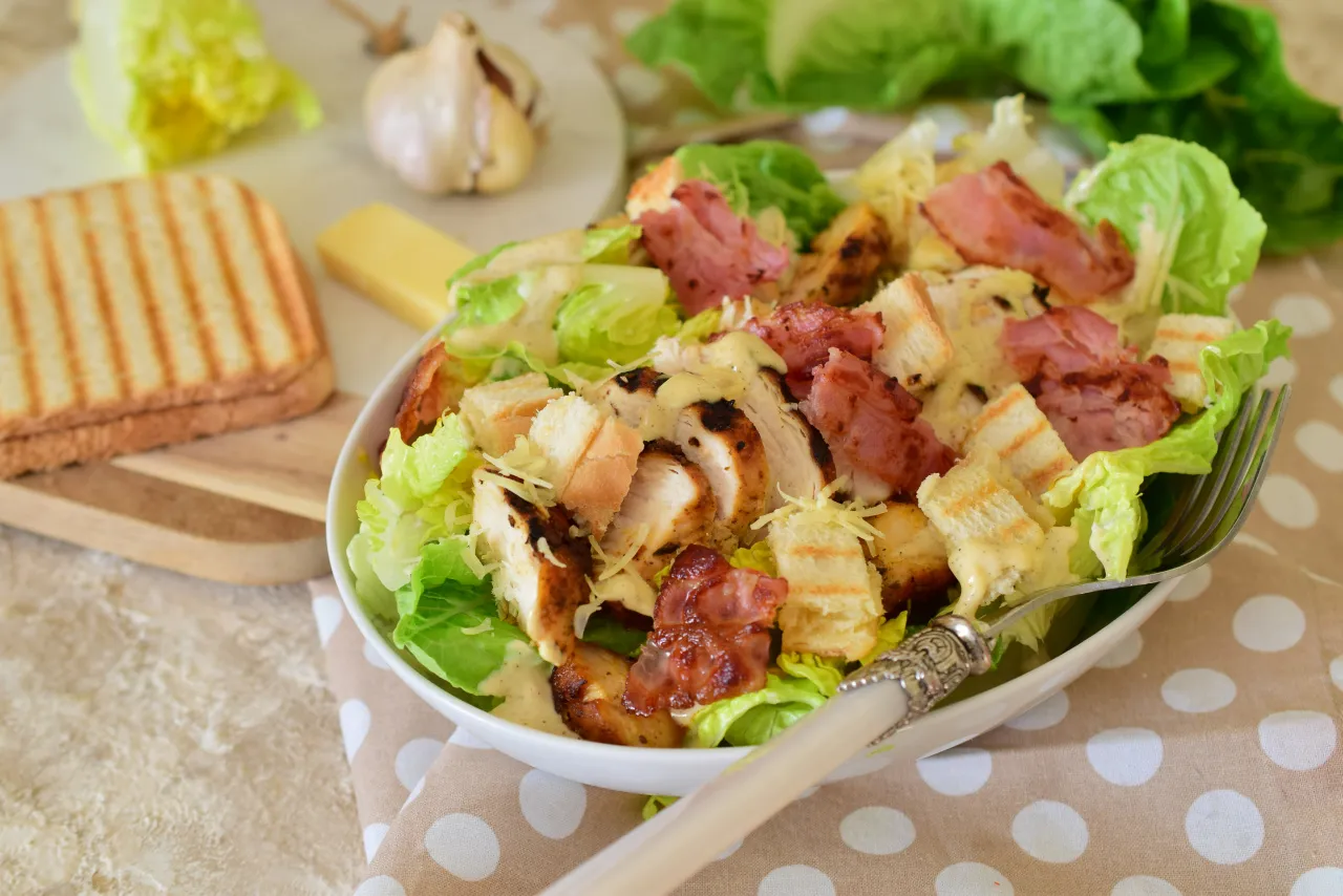Pyszna sałatka cezar z boczkiem, chrupiącymi grzankami i kurczakiem, polana kremowym sosem.