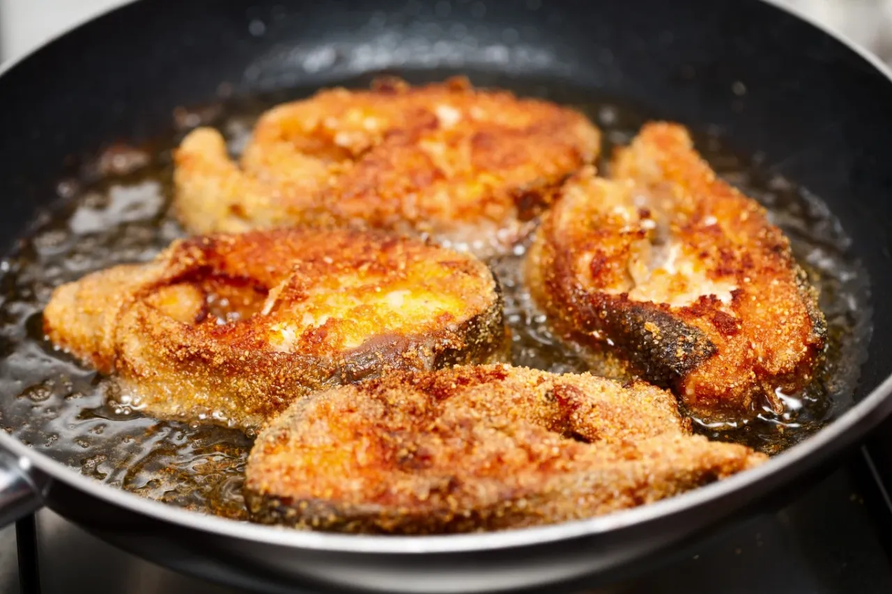 Chrupiące kawałki ryby w panierce smażą się na głębokim oleju na patelni. Idealny sposób, na czym smażyć rybę w panierce, by była złocista i pyszna.