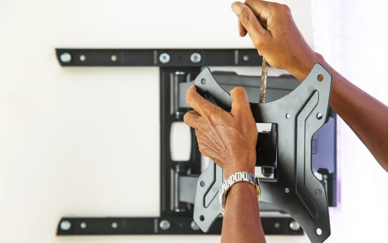 Ręce montują uchwyt do telewizora. Wkręcanie śruby to kluczowy etap, jak zamontować uchwyt do telewizora.
